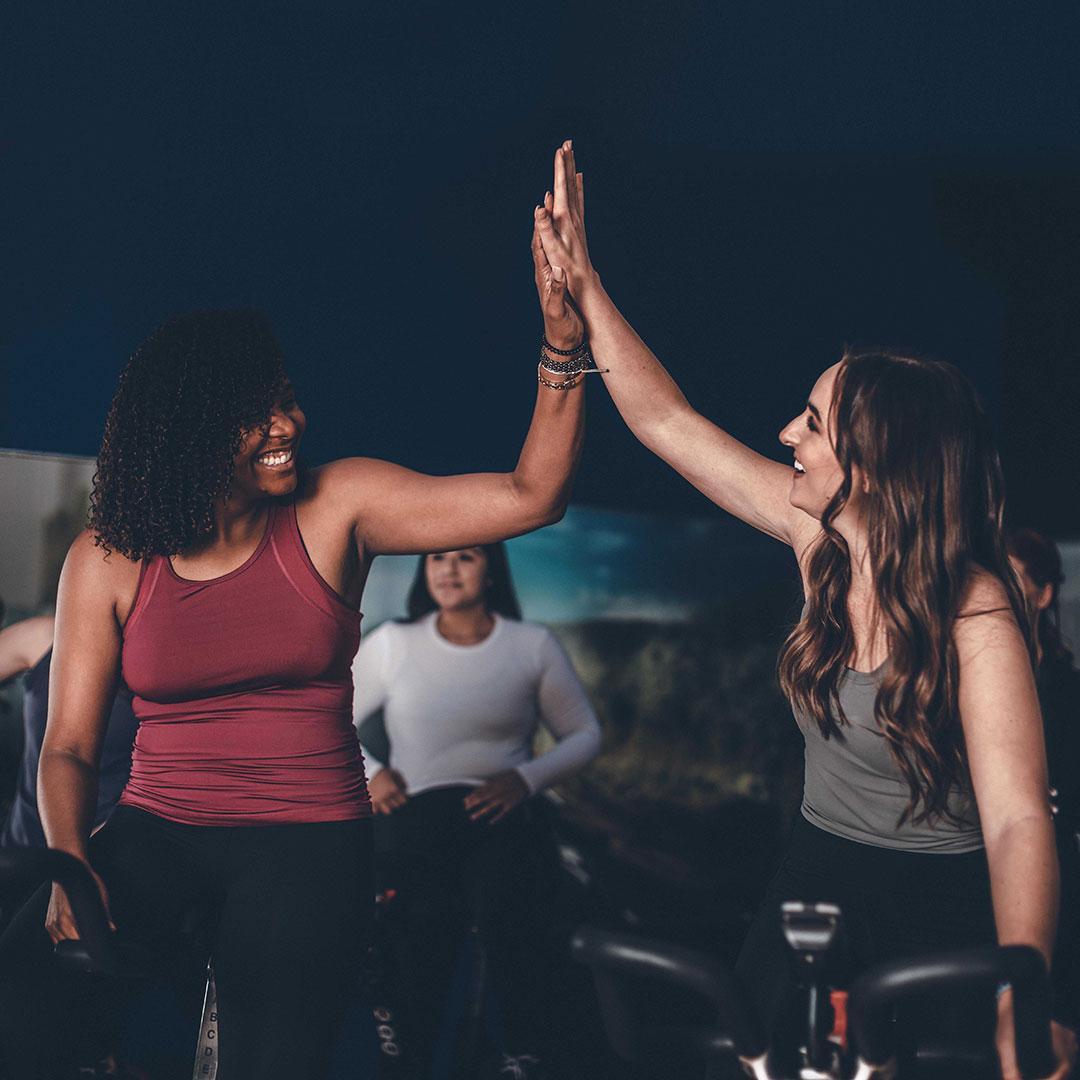 friends high-fiving in a cycle class