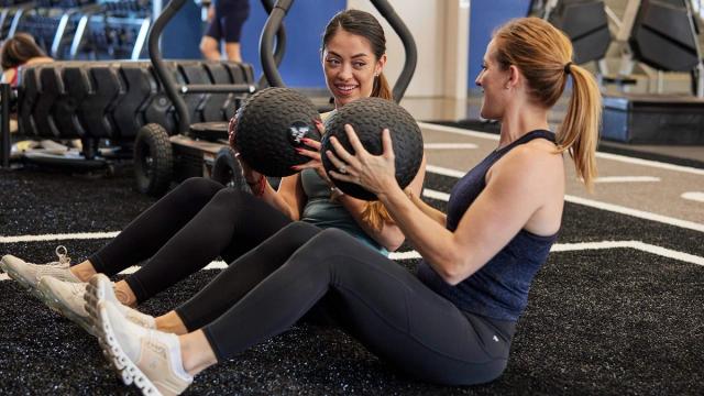 Two women training on turf with medicine balls